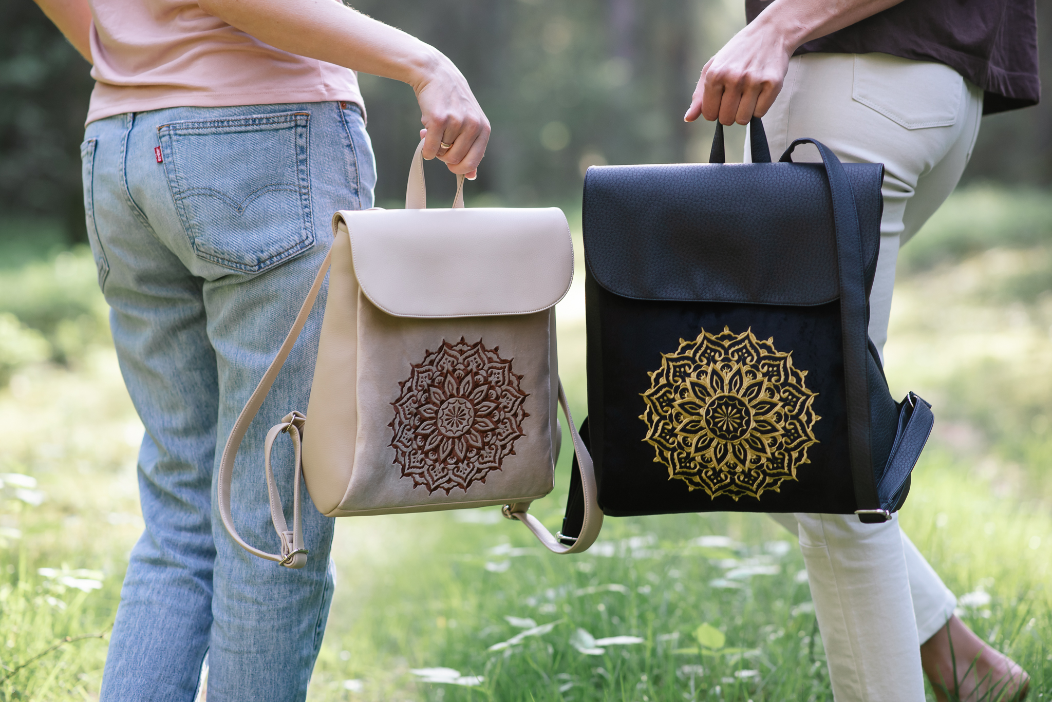 Šviesi ir juoda „Mandalos“ kolekcijos kuprinės su siuvinėtais ornamentais.
